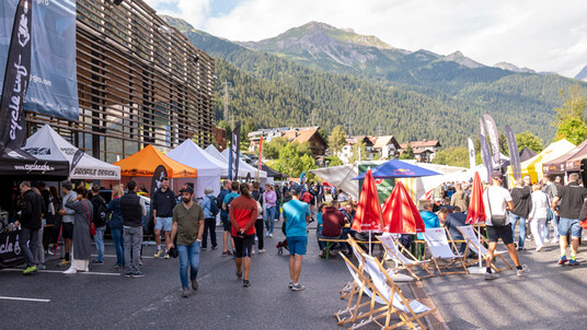 Buntes Markttreiben mit vielen Menschen, Ständen und Liegestühlen beim Arlberg Giro Wochenende