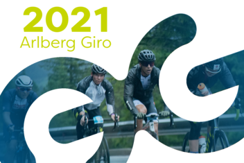 Racing cyclists at the Arlberg Giro 2021 master a tight bend. Forests and rocks can be seen in the background. ‘2021 Arlberg Giro’ is written in yellow/green at the top left of the picture.