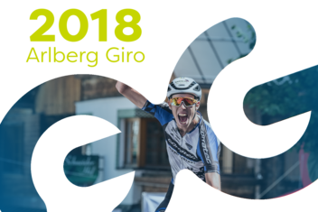 Racing cyclist cheers with a raised fist and is visibly shouting. ‘2018 Arlberg Giro’ is written in yellow/green at the top left of the picture.