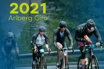 Racing cyclists at the Arlberg Giro 2021 master a tight bend. Forests and rocks can be seen in the background. ‘2021 Arlberg Giro’ is written in yellow/green at the top left of the picture.