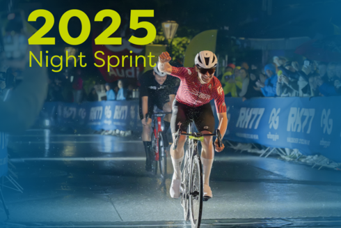 Racing cyclist races across the finish line in the rainy pedestrian zone of St. Anton, cheering - with a clenched fist - in front of many spectators. ‘2025 Night Sprint’ is written in yellow/green at the top left of the picture.