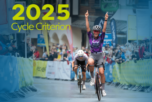 Racing cyclist cheering as she crosses the finish line in the village centre of St. Anton am Arlberg in front of a cheering audience. ‘2025 Cycle Criterion’ is written in yellow/green at the top left of the picture.