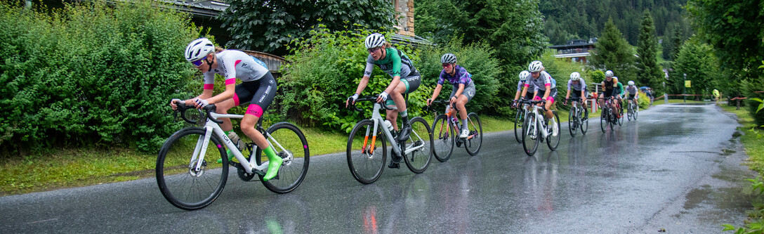 Professional female racing cyclists race through the green village of St. Anton am Arlberg in the rain. 