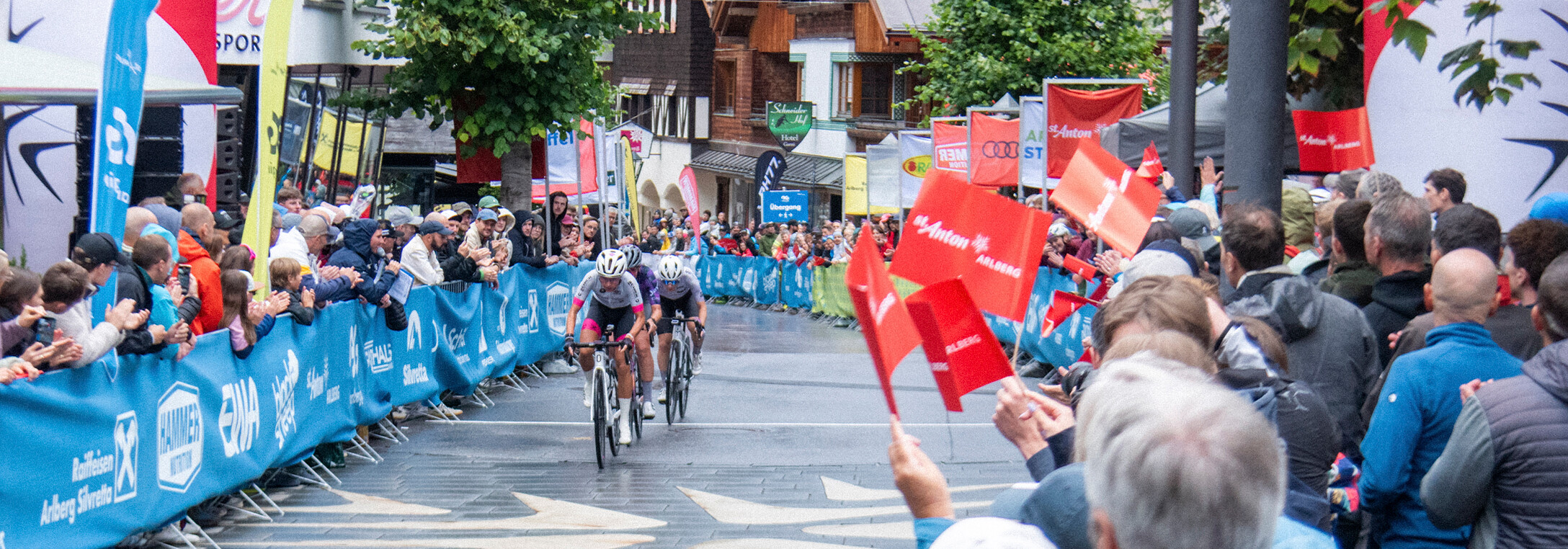 Professionelle Radfahrer fahren durch die Fußgängerzone in St. Anton am Arlberg. Fans feuern sie an. 